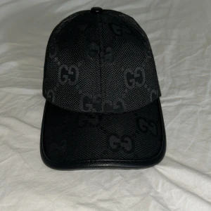 Svart keps från Gucci med GG-mönster - Snygg svart keps från Gucci med klassiskt GG-mönster över hela kepsen. Kepsen har justerbar rem baktill i skinn och böjd skärm med läderdetaljer. Tillverkad i slitstarkt material och har en riktigt clean och lyxig vibe. Pris kan diskuteras 