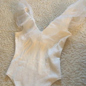 Body  - Superfin vit body med djup v-ringning och stora volangdetaljer i transparent tyg över axlarna. 🥰
