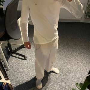 Vit långärmad tröja Tommy Hilfiger - Vit långärmad tröja från Tommy Hilfiger med liten broderad logga på bröstet. Tröjan är i mjuk bomull och har en klassisk, enkel design med rund hals. Perfekt för dig som gillar stilrena och tidlösa plagg.