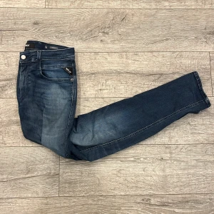 Replay Anbass jeans i mörkblå denim - Snygga Replay Anbass jeans i mörkblå tvätt med lätt slitning. Klassisk femficksmodell med smal passform och normal midja. Jeansen har dragkedjegylf och diskreta Replay-detaljer på fickan. Perfekta för dig som gillar stilrena och moderna jeans. | Storlek: 32/32 |