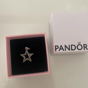 Pandora stjärnberlock i silver - Snygg stjärnformad berlock från Pandora i silverfärg. Berlocken har en öppen design med små glittrande stenar på ena sidan som ger extra bling. Perfekt att hänga på ett halsband eller armband för en cool och personlig touch.