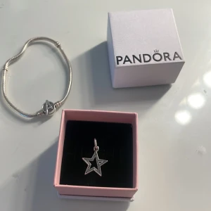 Pandora armband med stjärnberlock - Säljer ett snyggt silverfärgat armband från Pandora med en stjärnformad berlock. Armbandet har klassisk Pandora-låsning och berlocken är öppen i mitten med små detaljer längs kanterna. Perfekt att kombinera med andra smycken eller bära som den är.