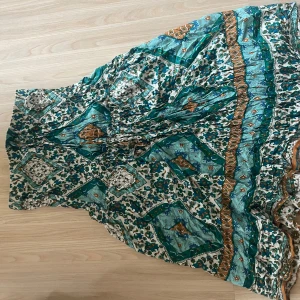 Grön och turkos långklänning med mönster - Säljer en flowy långklänning i grönt och turkost med bohemiskt mönster och inslag av vitt och brunt. Klänningen har ett avslappnat fall och är perfekt för varma dagar. Materialet känns lätt och svalt, och modellen är typisk för en Positano-klänning.