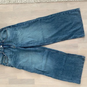 Wide jeans från H&M, blå, stl 38 - Säljer ett par blåa wide jeans från H&M i storlek 38. Jeansen har låg midja, klassisk femficksdesign och riktigt breda ben. Materialet är en mix av bomull och återvunnen bomull samt tencel. Perfekta för en avslappnad och trendig look.