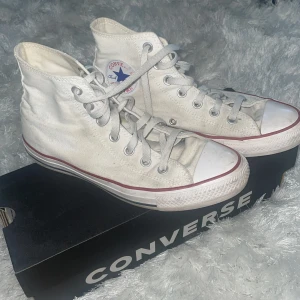 Converse  - Klassiska vita Converse Chuck Taylor All Star high-tops med röd och blå rand längs sulan. Jätte bra skick men lite dammiga eftersom dom inte används. Lite slitna på loggan (kolla bilden) men inget annat💗 Storlek 39  