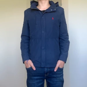 Marinblå vindjacka från Polo Ralph Lauren - Snygg marinblå vindjacka från Polo Ralph Lauren med röd broderad logga på bröstet. Jackan har dragkedja, hög krage och praktiska fickor. Perfekt för dig som vill ha en stilren och sportig look. Passar till både jeans och chinos. Jag köpte den för 2800Mitt pris är bara 1300!                Skickar inom 1-2 dagar,skriv till mig vid minsta fundering 😃       Mvh Emil 😀 