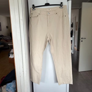 Beige jeansbyxor från Lindex Betty - Snygga beige jeansbyxor från Lindex Betty med klassisk femficksdesign och raka ben. Byxorna har bälteshällor, knapp och dragkedja framtill. Tillverkade i ett mjukt bomullstyg som känns skönt mot huden. Perfekta för en clean och stilren look.