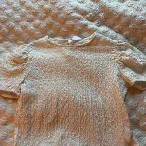 Vit blus med spetsdetaljer från Zara - Supersöt vit blus från Zara med korta puffärmar och elastisk struktur. Ärmarna har unika virkade spetsdetaljer med blommönster. Perfekt för dig som gillar romantiska och detaljerade plagg. Rund halsringning och knäppning bak i nacken.