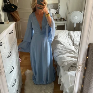 Ljusblå långklänning med vida ärmar - Superfin ljusblå långklänning med djup v-ringning, markerad midja och vida, flowiga ärmar. Klänningen har en slits framtill och är perfekt för bal, bröllop eller andra festligheter!😍 för lång på mig som är ca 165 cm och lite stor i bysten på mig med liten byst.💞 oanvänd, lappen sitter kvar.