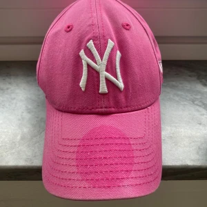 Rosa New Era Yankees keps 9FORTY - Snygg rosa New York Yankees keps från New Era, modell 9FORTY. Kepsen har böjd skärm, broderad vit NY-logga framtill och New Era-logga på sidan. Tillverkad i 100% bomull för en skön och luftig känsla. Perfekt accessoar för att lyfta din stil.