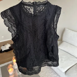 Svart spetsblus från ONLY - Supersnygg svart blus från ONLY med detaljerad spets och volangkantade ärmhål. Blusen är ärmlös och har en  rund halsringning. 💕