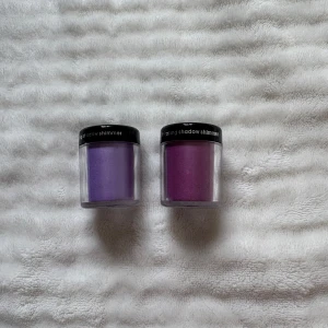 Lila och rosa shimmerögonskuggor - Två burkar lösa ögonskuggor från Cosmobeauty i nyanserna lila (No. 7) och rosa-lila (No. 19). Båda har intensivt skimmer och kommer i genomskinliga plastburkar med svart lock. Perfekta för att skapa färgstarka och glittriga ögonlooks.