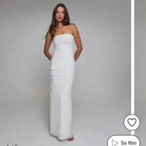 Vit axelbandslös långklänning - Säljer en snygg vit axelbandslös långklänning med tight passform från Nelly. Klänningen har ett unikt ribbat strukturmönster över hela tyget. Den är figurnära och har en stilren, modern look från 2024. Aldrig använd!