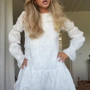Vit klänning Nakd - Säljer min helt nya vita klänning med blommigt mönster och volangdetaljer🥰 Klänningen har långa armar och en luftig passform, perfekt för sommaren. 💞💞 