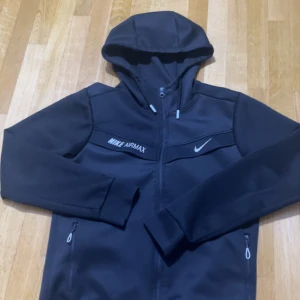 Svarta Nike Air Max mjukisbyxor M - Svarta mjukisbyxor från Nike Air Max med snygga vita loggor på låret. Byxorna har dragkedjor vid fickorna och är tillverkade i ett mjukt och stretchigt material som passar perfekt för chill eller träning. Snygg, sportig look med smal passform.