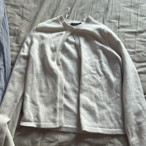 Vit kofta från Gina Tricot - Mysig vit kofta från Gina Tricot i storlek S. Koftan har rund halsringning, ribbade kanter och stängs med en knapp upptill. Perfekt att slänga över en topp för en enkel och clean look.