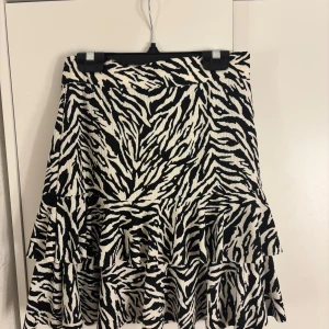 Somrig mönstrad volangkjol  - Supersnygg kort kjol från Ambar med svartvitt zebramönster och volangdetaljer. Kjolen har en lätt strukturerad yta och är perfekt för dig som vill sticka ut. Resår i midjan för skön passform. Den är helt oanvänd. Perfekt att ha på sommaren! Vid frågor är det bara att höra av sig💞