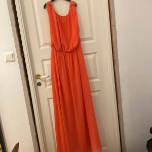 Lång rosa orange klänning från Bik Bok - Snygg långklänning i rosa orange från Bik Bok. Klänningen har djup v-ringning i ryggen, resår i midjan och är ärmlös. Tillverkad i ett lätt, flowy syntetmaterial som ger en luftig känsla. Perfekt för sommarens alla tillfällen. Har en tråd som gått upp under armen på ena sidan. Pris kan diskuteras!