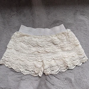 Vita spetsiga shorts med volang - INTRESSESKOLL! Superfina vita shorts med spets och volangdetaljer. De har elastisk midja i glittrigt tyg. Har en defekt vid grenen därav priset❣️