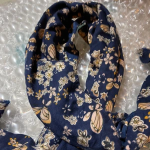 Blommig marinblå halsduk i bomull - Snygg marinblå halsduk med blommigt mönster i beige, vitt och gult. Tunt och mjukt material, perfekt att slänga över axlarna eller vira runt halsen. Fransen i kanterna ger en avslappnad vibe och den blommiga designen gör den extra charmig.