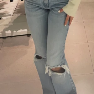 Ljusblå ripped jeans från Pull&Bear - Säljer ett par ljusblå jeans från Pull&Bear med snygga slitningar och hål vid knäna. Jeansen har mid midja, raka ben och råa kanter upptill för en extra edgy vibe. Perfekta för dig som gillar en avslappnad och trendig look.