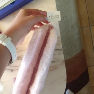 Rosa fluffigt pennskrin Butterfly - Supersöt ljusrosa pennskrin i fluffigt syntetmaterial med broderad text 'Butterfly' och en glittrig fjäril på framsidan. Väskan har dragkedja och en matchande rosa handledsrem. Perfekt för att bära småsaker och ge din look en gullig touch.