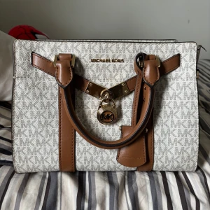 Michael Kors handväska  - Snygg handväska från Michael Kors i beige med bruna detaljer och guldiga metalldetaljer.