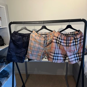 Rutig shorts med snörning - Tre par snygga shorts med elastisk midja och snörning. Ett par är marinblå med diskret rutmönster, de andra två har klassiskt beige rutigt mönster med svarta, vita och röda linjer. Perfekta för sommaren och riktigt sköna att bära. Materialet känns lätt och luftigt.