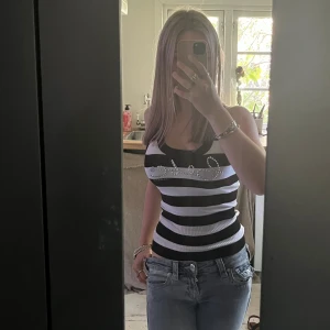 Randig ribbad linne från Bebe - Säljer ett svartvitt ribbat linne från Bebe med breda ränder och glittrande strassdetaljer på bröstet där det står 'bebe'. Sitter tight och har en croppad känsla, perfekt till jeans eller kjol. Supersnygg och trendig topp för dig som gillar statement-plagg.