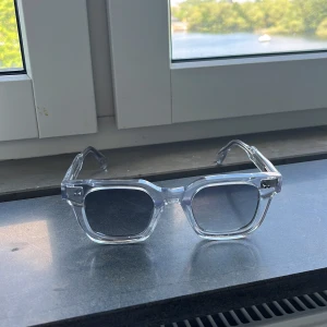 CHIMI solglasögon - Snygga solglasögon från CHIMI med transparent, fyrkantig båge i plast och mörka glas. Kommer med originaletui och box. Perfekt accessoar för att lyfta din stil med en modern och clean look.