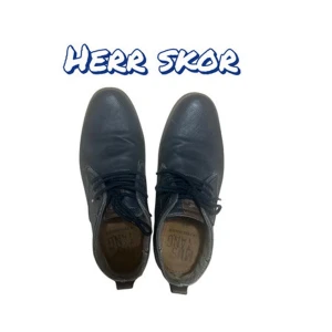 Mörkblå herrskor från Mustang - Snygga mörkblå herrskor från Mustang med klassisk design. Skorna har snörning, rund tå och är tillverkade i skinn med perforerade detaljer på sidorna. Vit sula med Mustang-logga på sidan ger en sportig touch. Perfekta för en stilren look.