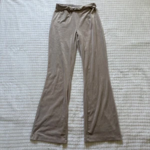 Low waist mjukisbyxor från Gina Tricot - Supermjuka beiga mjukisbyxor från Gina Tricot i velour-liknande material. Byxorna har hög midja med öljetter för snörning, vida ben och två bakfickor. Perfekta för en chill och avslappnad look. 