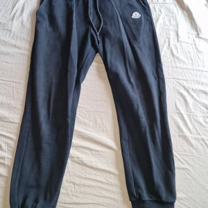 Svarta mjukisbyxor från Moncler - Svarta mjukisbyxor från Moncler med dragsko i midjan och ribbade muddar vid bensluten. Byxorna har en broderad Moncler-logga på höften och är tillverkade i mjukt material. 