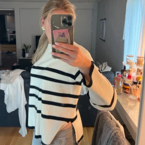 Randig vit och svart stickad tröja - Säljer en oversized stickad tröja i vitt med svarta horisontella ränder. Tröjan har lång ärm, rund halsringning och slits i sidorna. Perfekt för dig som gillar en chill och trendig look med lite extra volym i passformen.