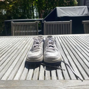 Nike Air Force 1 vita och svarta sneakers - Säljer ett par klassiska Nike Air Force 1 sneakers i vitt och svart skinn. Skorna har lågt skaft, rund tå, snörning och den ikoniska swoosh-loggan på sidorna. Perfekta för dig som gillar streetstyle och vill ha en tidlös sneaker med cool kontrast mellan vitt och svart. Storlek 38 men passar 38,5 