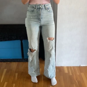 Ljusblå ripped jeans från H&M, strl 34 - Säljer ett par ljusblå jeans från H&M i storlek 34. De är högmidjade med raka ben och har snygga slitningar och hål på båda knäna. Sitter väldigt bra i både midja, ben och rumpa. (De är lite skrynkliga då de har legat vikta men det går bort om man stryker dem.)🩵
