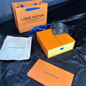Svart LV bälte - Säljer ett svart Louis Vuitton bälte i skinn med klassiskt LV-monogram i grått. Bältet har en stilren design med bred rem och tydlig logga, perfekt för att lyfta vilken outfit som helst. Kommer med originalförpackning, dustbag och påse.