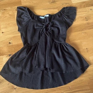 Svart blus med snörning, från lager 157 - Supersöt svart blus från lager 157 med volangärmar och snygg snörning framtill. Blusen har en lätt rynkad struktur och är lite längre baktill för en flowy look. 