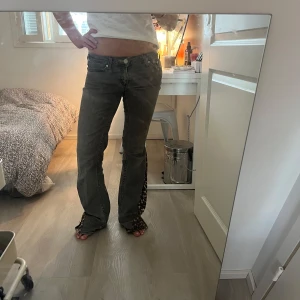 Grå bootcut jeans med leoparddetalj - Unika grå jeans med bootcut passform och låg midja. Nedtill har byxorna en cool leopardmönstrad panel som sticker ut och ger extra edge. Jeansen har klassisk femficksdesign och råa kanter vid bensluten. Perfekta för dig som vill sticka ut lite extra.