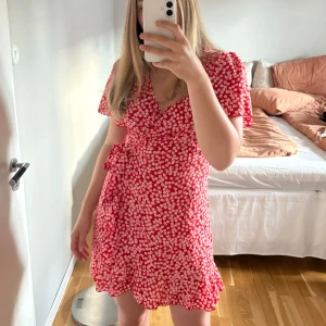Röd blommig omlottklänning - En röd miniklänning med vita blommor. Omlott och knyts i midjan. Storlek M men passar säkert S också.  Använd några gånger men är i mycket bra skick🤗