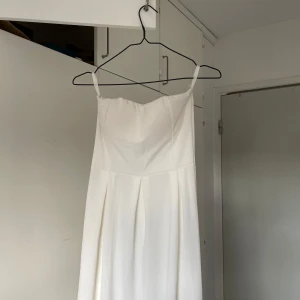 Vit långklänning  - En stilren vit långklänning som en enkel, elegant design med veck framtill och är axelbandslös upptill. Perfekt för dig som vill ha en clean och klassisk look.