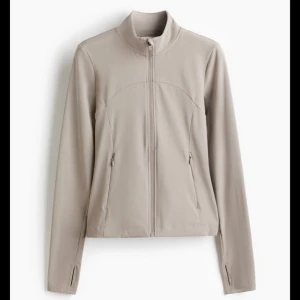 Beige sportig vindjacka med dragkedja - Snygg beige vindjacka med hel dragkedja och hög krage. Jackan har långärmad design med tumhål vid ärmsluten och smickrande passform. Perfekt för en aktiv livsstil och enkel att matcha med träningskläder eller jeans. Köpte den för 500kr