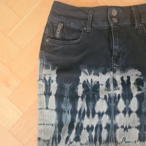 Tie-dye jeanskjol från Culture - Cool jeanskjol från Culture i blått och vitt tie-dye-mönster. Kjolen har klassiska jeansdetaljer som fickor fram och bak, bälteshällor och dubbla knappar i midjan. Snygg och unik look som sticker ut.