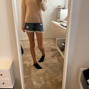 Blå jeansshorts med spetskant - Snygga blå jeansshorts med slitna detaljer och vit spetskant längst ner. Klassisk femficksmodell med knapp och dragkedja framtill. Perfekta för sommaren och ger en cool, avslappnad vibe med en söt twist tack vare spetsen.