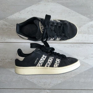 Adidas Campus 00s Black Leopard sneakers - Svarta Adidas Campus 00s sneakers med ikoniska leopardmönstrade ränder i beige och svart i storlek 39 1/3. Skorna har en beige sula, svarta skosnören och detaljer i mocka. Perfekt för dig som vill sticka ut med en cool och trendig look. De är sparsamt använda, alltså i bra skick förutom att mockan är något missfärgad och lite smuts på de leopardmönstrade ränderna. De är köpta från soleplus för 2499kr (se på sista bilden), mitt pris är 1099kr. Men priset går att diskuteras!💓
