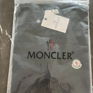 Svart Moncler t-shirt med logga - Svart t-shirt från Moncler med klassisk rund hals och liten broderad logga på bröstet. Enkel och stilren design som passar perfekt till jeans eller shorts. Tillverkad i mjuk bomull för en skön känsla hela dagen.