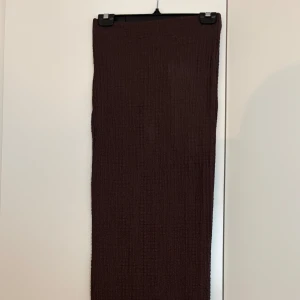 Brun långkjol i strukturerad bomull - Mörkbrun långkjol med rak passform och vågig kant nertill. Kjolen är tillverkad i ett strukturerat bomullstyg som ger en cool och avslappnad vibe. Perfekt för dig som gillar stilrena plagg med lite edge. Aldrig använd.