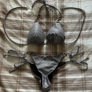 Bikini från Calzedonia - Helt oanvänd bikini ifrån Calzedonia! Svart & vit randig med glittrig laminering på tyget. Guldiga detaljer. Knyts runt nacken och runt ryggen. Trosan har scrunch där bak (se bild 2). Jag har klippt bort alla lappar tyvärr då jag tänkte ha på mig den, men så blev det inte.! Storlek S på överdelen och storlek XS på underdelen. Original pris för båda är 800.