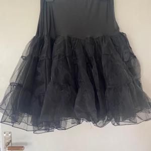 Svart volangkjol i tyll - Säljer en svart underkjol med flera lager volanger i tyll. Kjolen har en fluffig look som ger extra volym och passar perfekt under en klänning med vidd. Resår i midjan för skön passform.