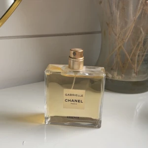 Chanel Gabrielle Essence 50ml parfym - Chanel Gabrielle Essence parfym i en stilren, fyrkantig glasflaska med guldfärgad spraykork. Flaskan rymmer 50 ml och har en ljusgul vätska. Klassisk och elegant design med tydlig Chanel-logga på etiketten.